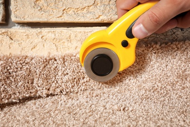 Photo of Man cutting new carpet flooring indoors, closeup