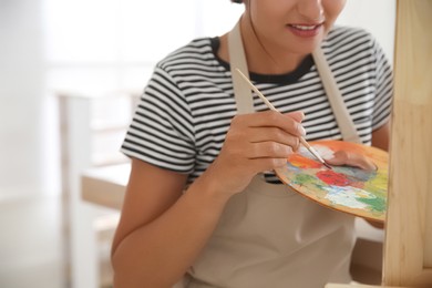 Photo of Young woman drawing on canvas indoors, closeup