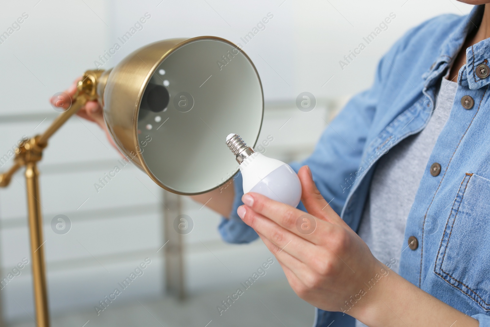 Photo of Woman changing light bulb in lamp indoors, closeup