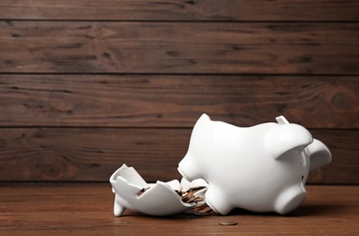 Broken piggy bank with coins on wooden table