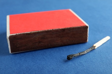 Photo of Red box and burnt match on color background, closeup
