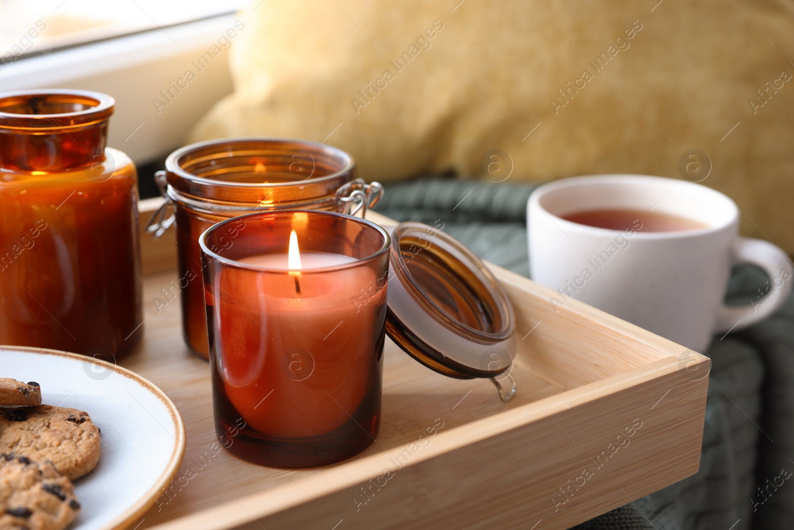 Photo of Tray with burning candles and cookies on windowsill indoors