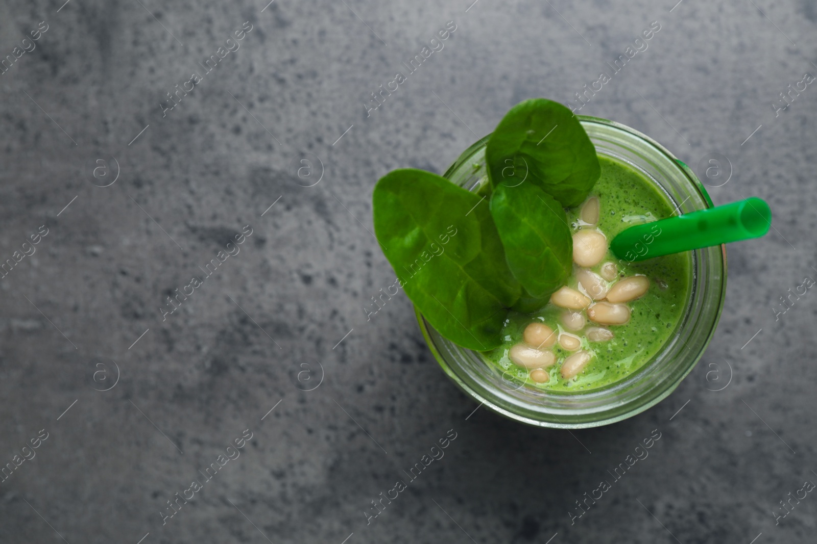 Photo of Jar of healthy green smoothie with fresh spinach on grey table, top view. Space for text