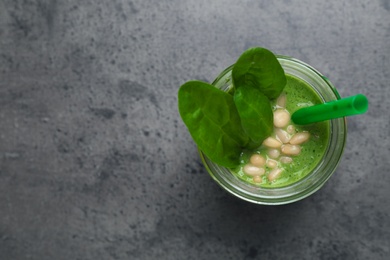 Jar of healthy green smoothie with fresh spinach on grey table, top view. Space for text