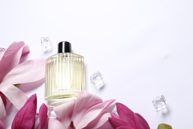 Beautiful magnolia flowers, bottle of perfume and ice cubes white background, above view. Space for text