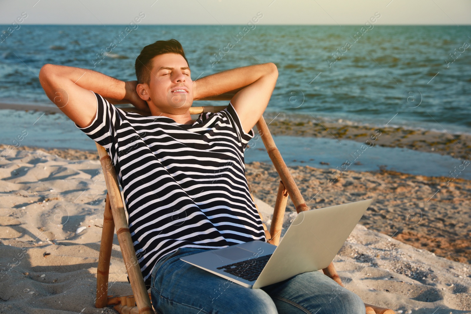 Photo of Man with laptop relaxing in deck chair on beach