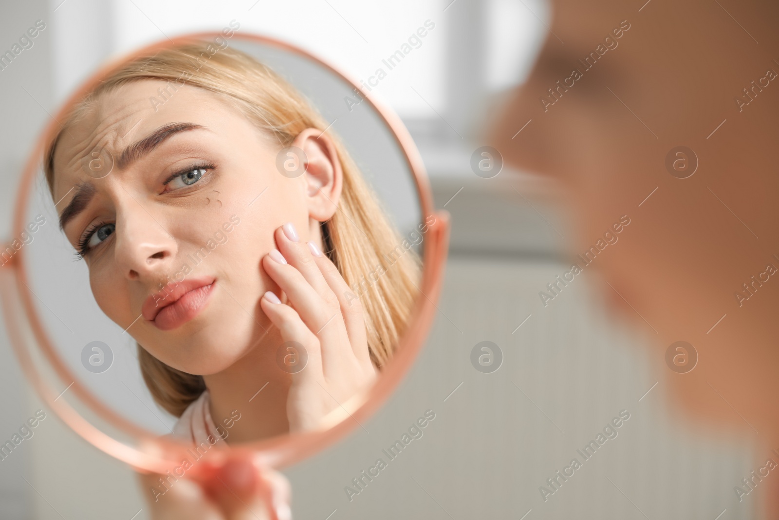 Photo of Young woman with eyelash loss problem looking in mirror indoors