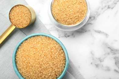 Photo of Brown sugar in bowls and scoop on white marble table, top view