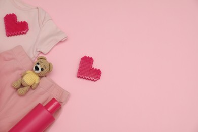 Photo of Bottle of laundry detergent, baby clothes, toy bear and decorative hearts on pink background, flat lay. Space for text