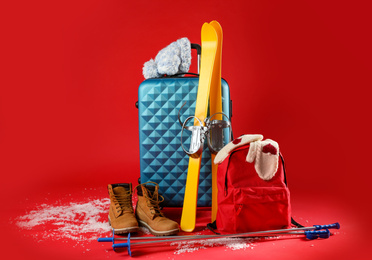 Photo of Suitcase with warm clothes and skis on red background. Winter vacation