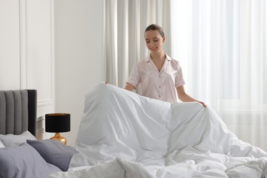 Photo of Young beautiful woman making bed in room