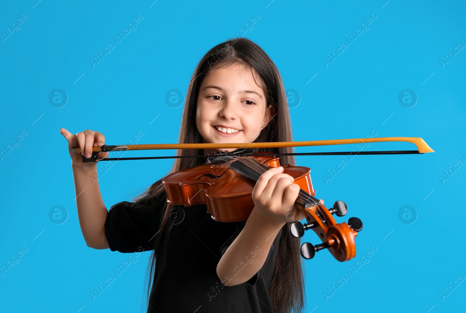 Photo of Preteen girl playing violin on light blue background