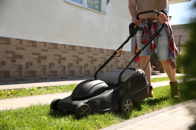 Photo of Man cutting green grass with lawn mower on backyard, closeup