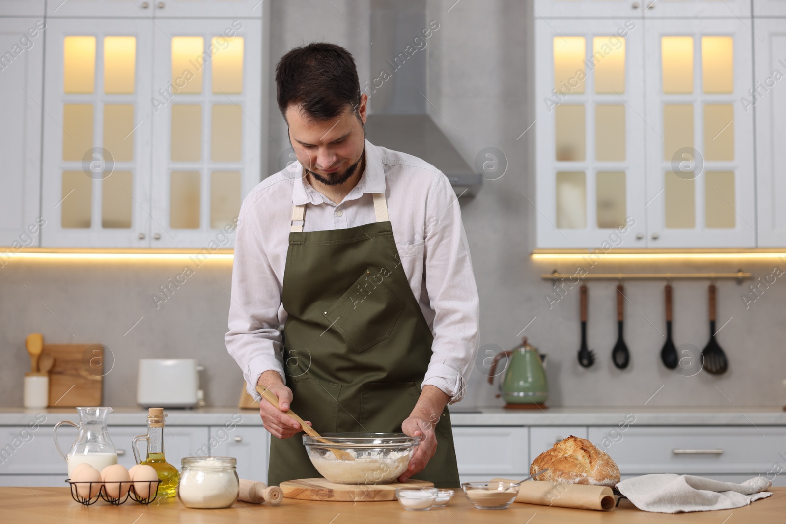 Photo of Making bread. Man preparing dough in bowl at wooden table in kitchen