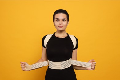 Beautiful woman with orthopedic corset on orange background