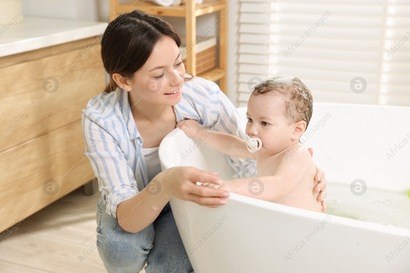 Photo of Mother bathing her cute little baby in tub at home