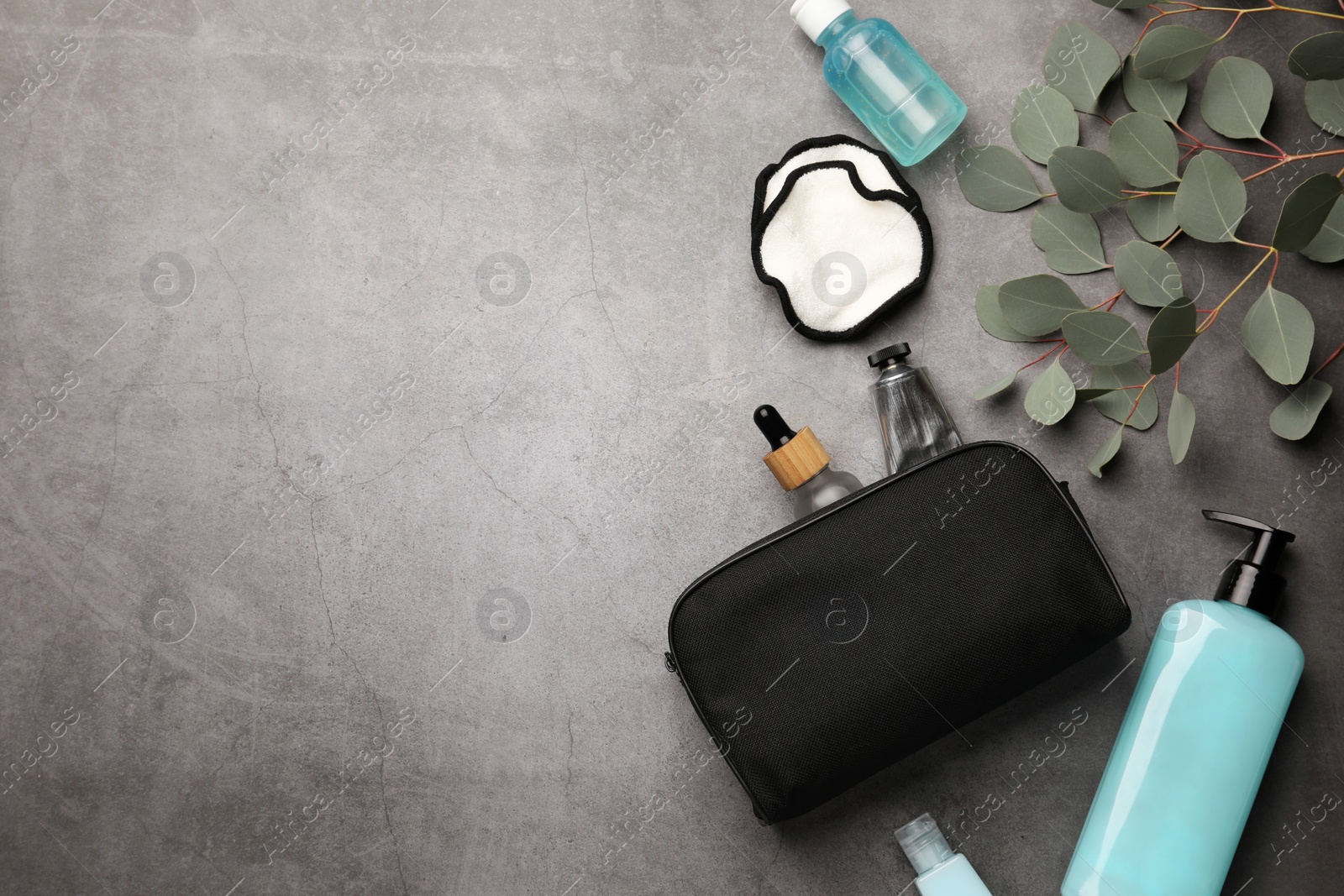 Photo of Preparation for spa. Compact toiletry bag, different cosmetic products and eucalyptus on grey textured background, flat lay. Space for text