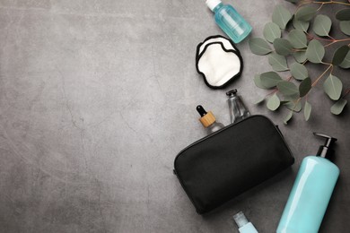 Preparation for spa. Compact toiletry bag, different cosmetic products and eucalyptus on grey textured background, flat lay. Space for text