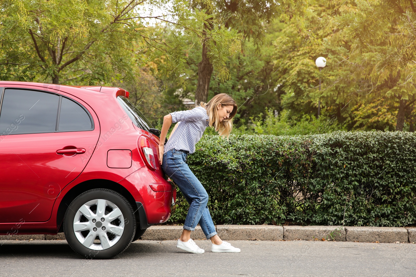 Photo of Woman pushing broken car on road along city street