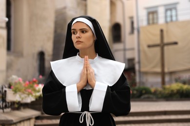 Photo of Young nun with hands clasped together praying near building outdoors