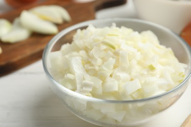 Chopped onion in bowl on white wooden table, closeup