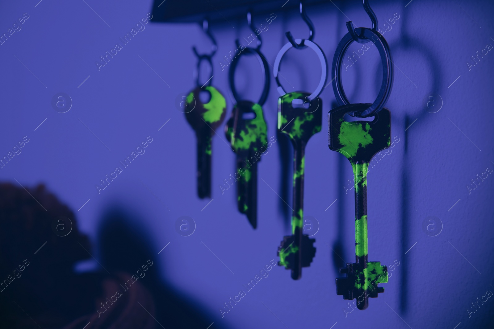 Image of Holder with different keys on wall, view under UV light. Sanitizing objects during coronavirus outbreak