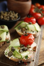 Photo of Bruschettas with capers, vegetables and cream cheese served on wooden board, closeup