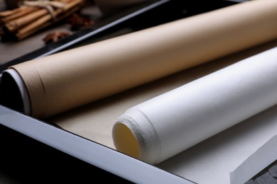 Photo of Rolls of parchment paper in baking pan on table, closeup