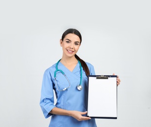 Portrait of medical assistant with stethoscope and clipboard on light background. Space for text