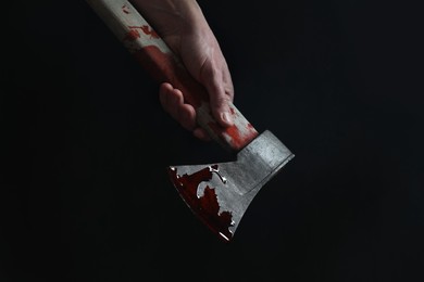 Man holding bloody axe on black background, closeup