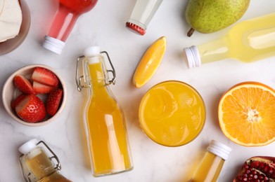 Tasty kombucha in bottles, glass and fresh fruits on white marble table, flat lay