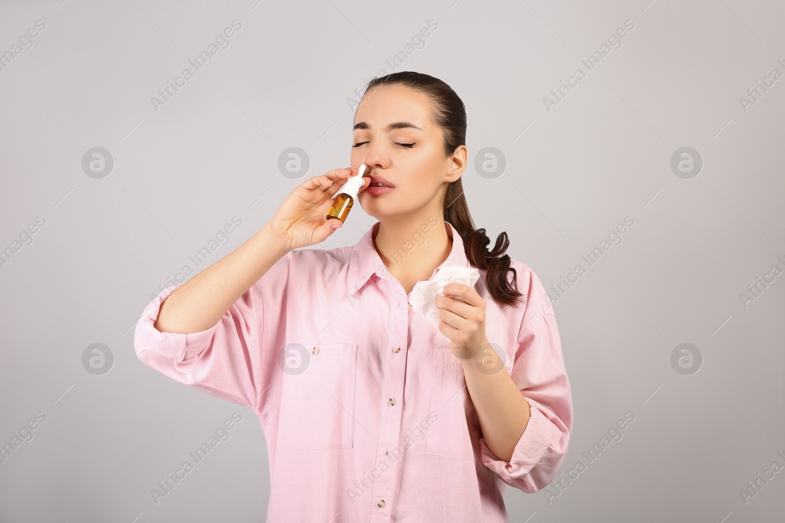 Photo of Woman using nasal spray on light grey background