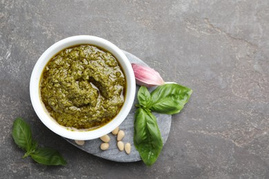 Photo of Tasty pesto sauce in bowl, basil, pine nuts and garlic on grey table, top view. Space for text