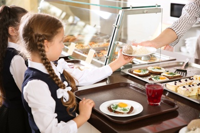 Photo of Woman giving plate with healthy food to girl in school canteen