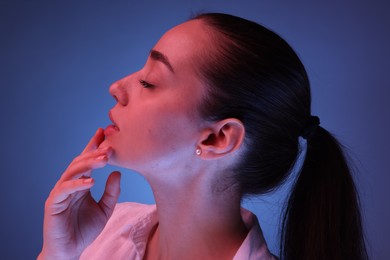 Portrait of beautiful young woman posing on blue background with neon lights