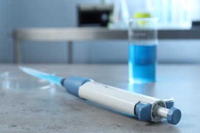 Laboratory analysis. Micropipette, petri dish and beaker with liquid on grey table, closeup