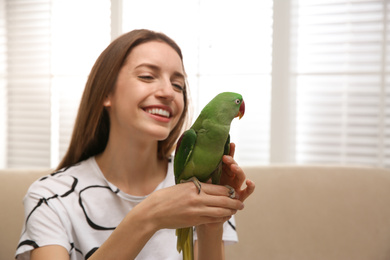 Photo of Young woman with cute Alexandrine parakeet indoors