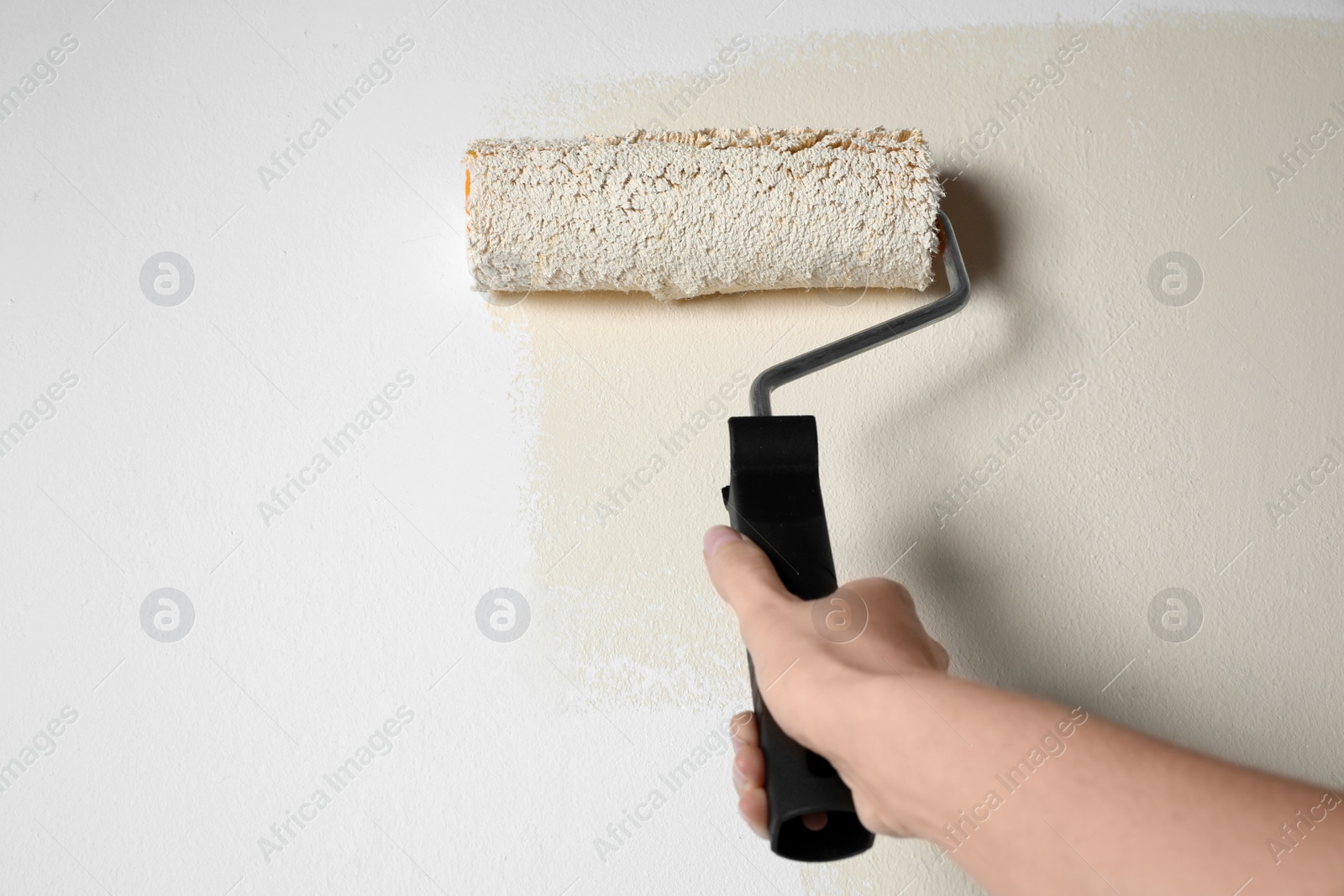 Photo of Woman painting white wall with beige dye, closeup