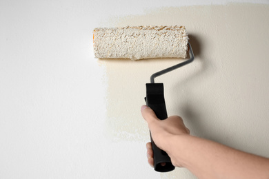 Photo of Woman painting white wall with beige dye, closeup