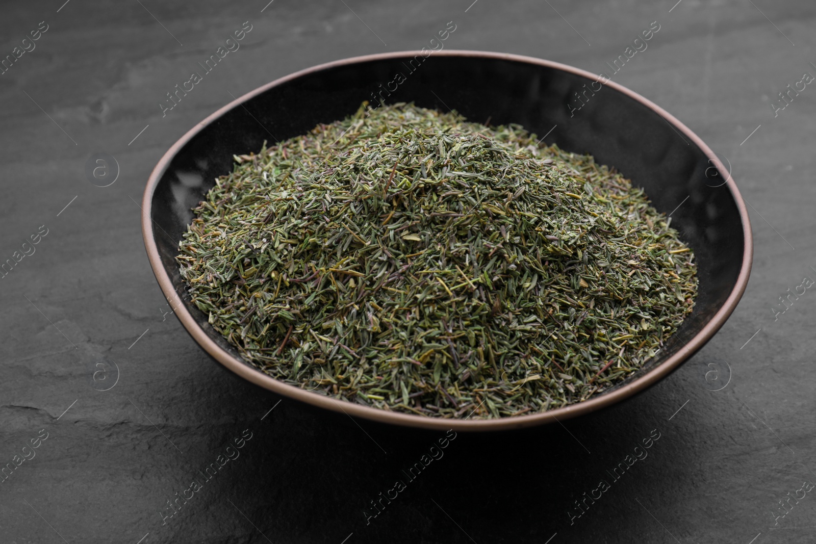 Photo of Bowl with dried thyme on black table, closeup