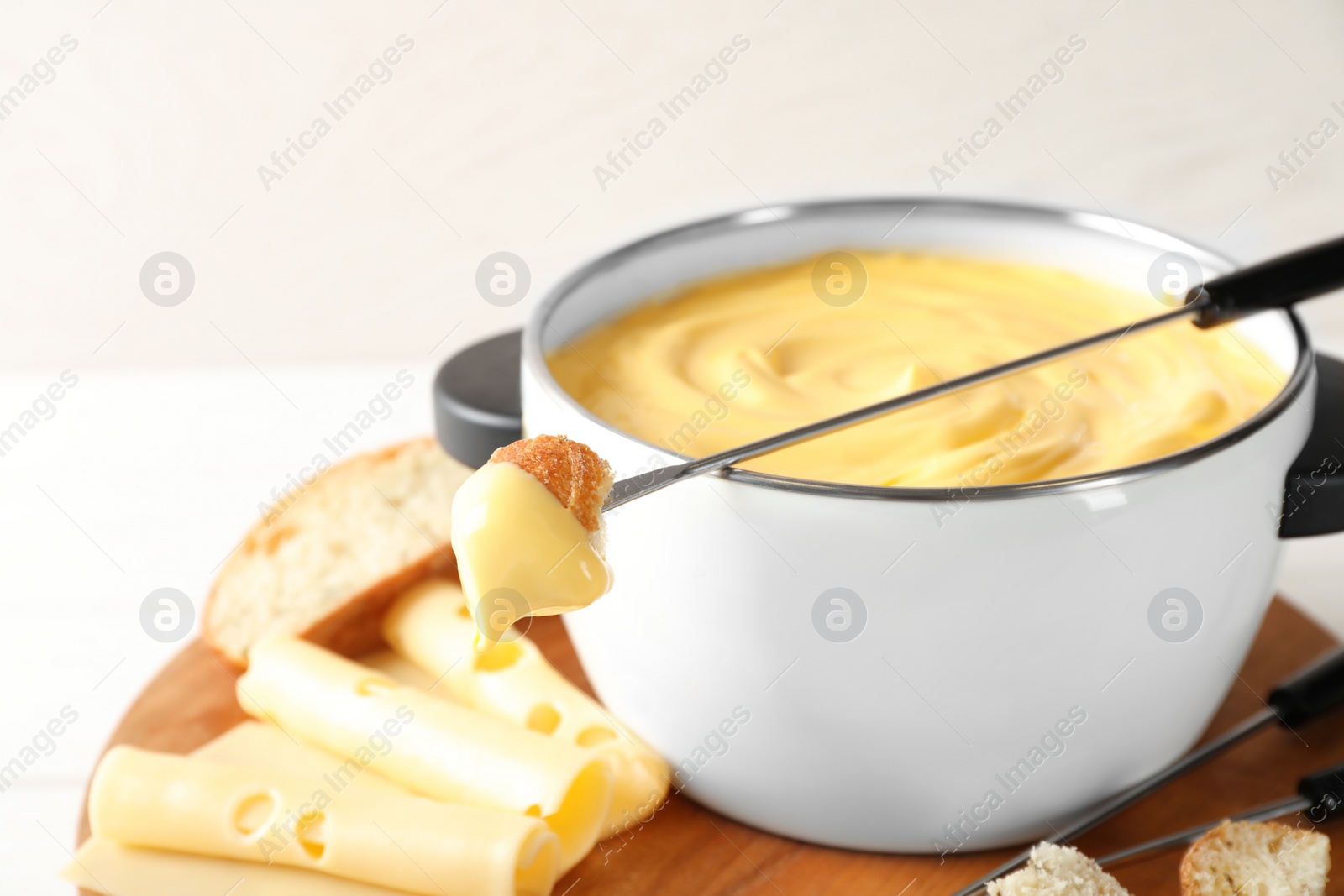 Photo of Pot of delicious cheese fondue and fork with bread on table