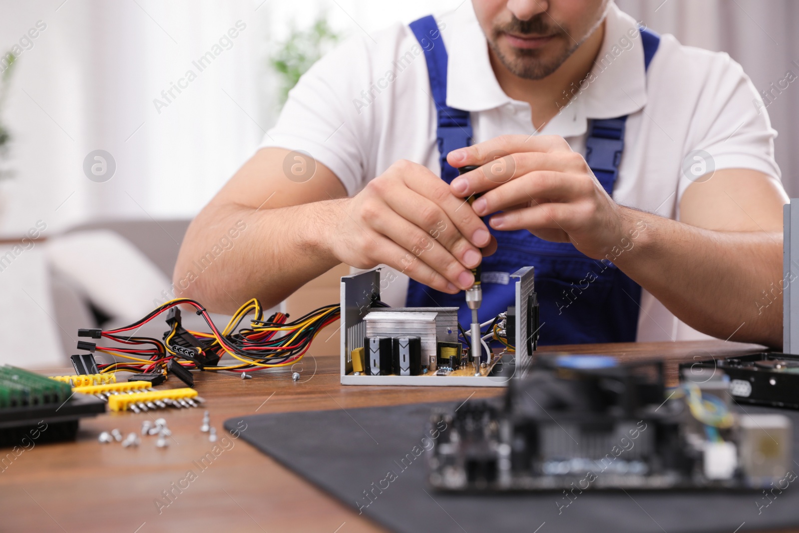 Photo of Male technician repairing power supply unit at table indoors, closeup