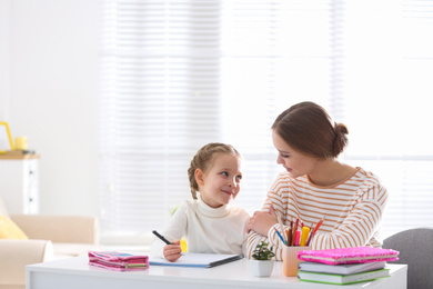 Photo of Woman helping her daughter with homework at table indoors