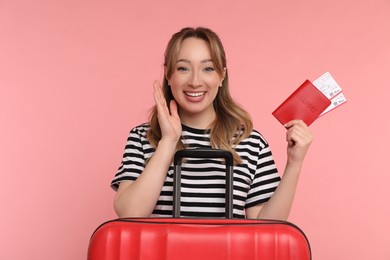 Photo of Happy young woman with passport, ticket and suitcase on pink background