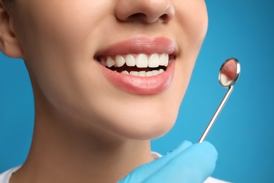 Photo of Doctor examining woman's teeth on blue background, closeup. Cosmetic dentistry