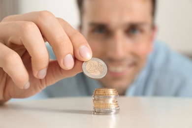 Photo of Young smiling man stacking coins at table, focus on hand