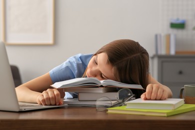 Young tired woman sleeping near books at wooden table indoors