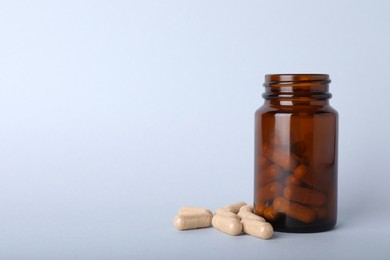 Photo of Gelatin capsules and bottle on light grey background, space for text