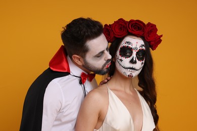 Photo of Couple in scary bride and vampire costumes on orange background. Halloween celebration