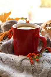 Cup of hot drink and autumn leaves on knitted sweater. Cozy atmosphere